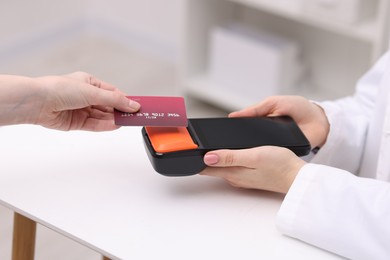 Photo of Woman paying with credit card via terminal at counter indoors, closeup