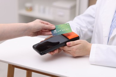 Photo of Woman paying with credit card via terminal at counter indoors, closeup