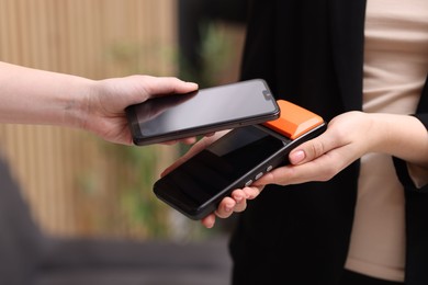 Photo of Woman paying with smartphone via terminal against blurred background, closeup