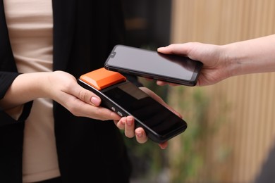 Photo of Woman paying with smartphone via terminal against blurred background, closeup