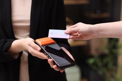 Photo of Woman paying with credit card via terminal against blurred background, closeup