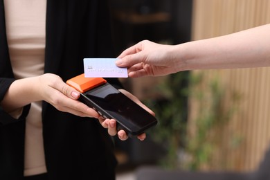 Photo of Woman paying with credit card via terminal against blurred background, closeup