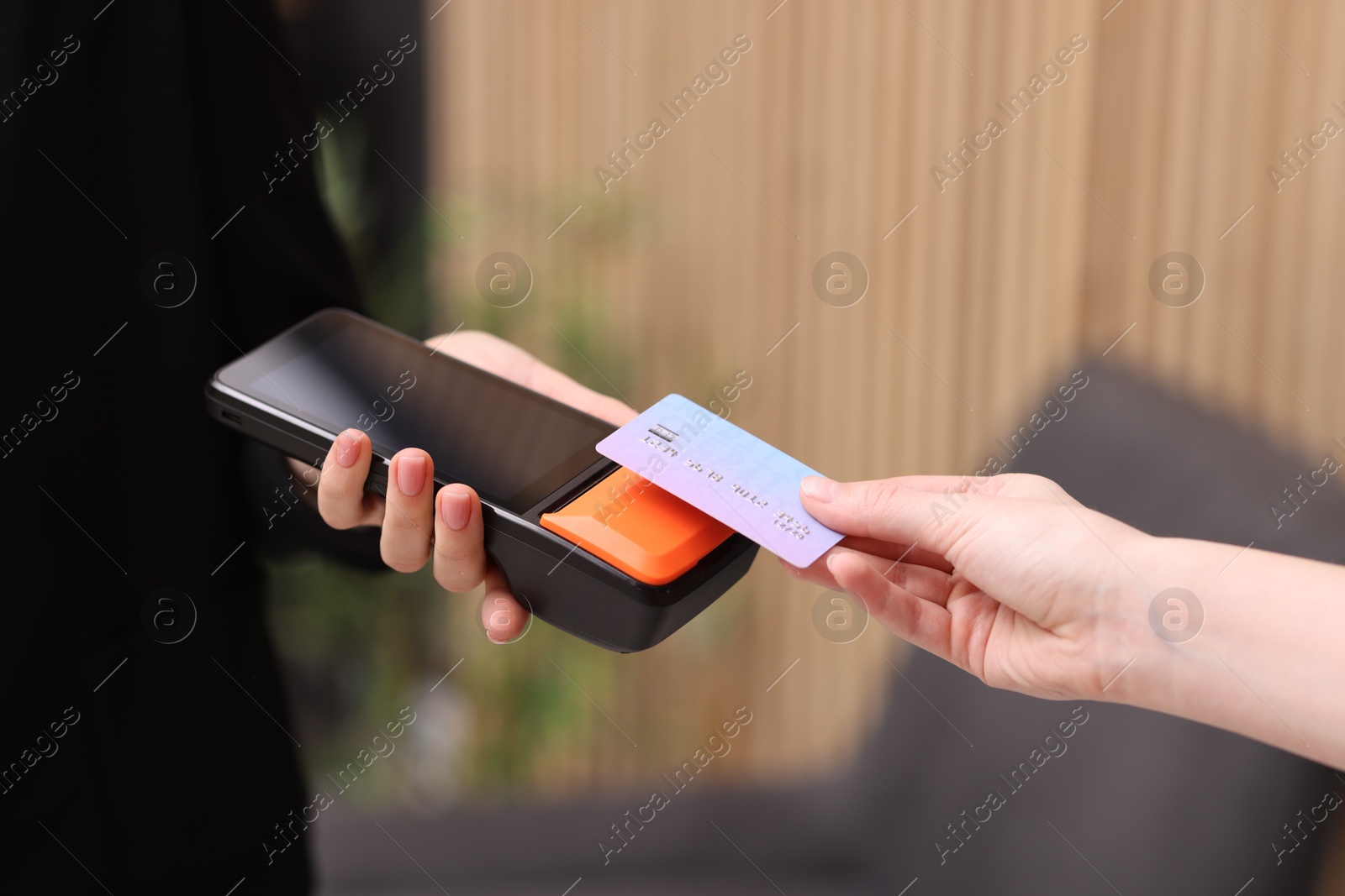 Photo of Woman paying with credit card via terminal against blurred background, closeup