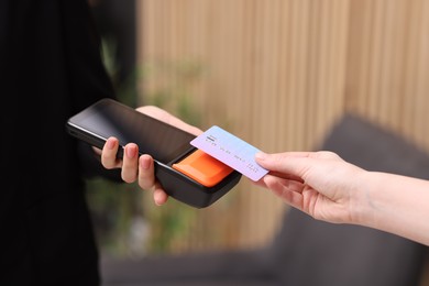 Photo of Woman paying with credit card via terminal against blurred background, closeup