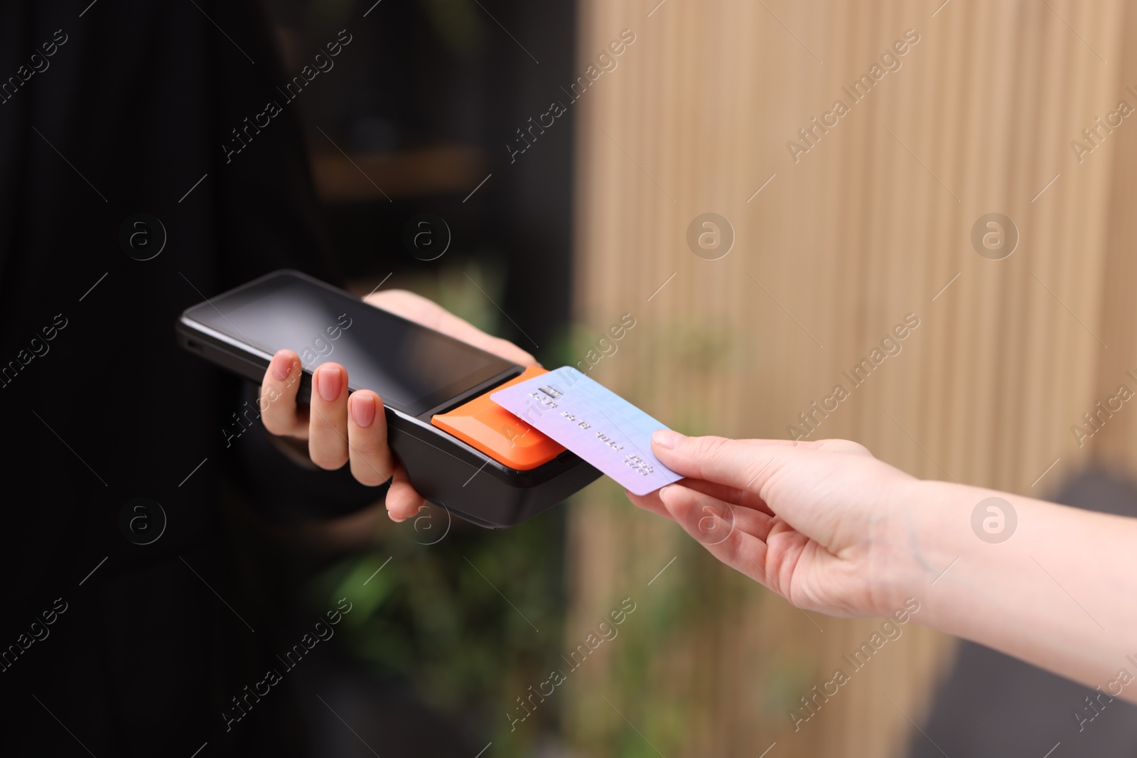 Photo of Woman paying with credit card via terminal against blurred background, closeup