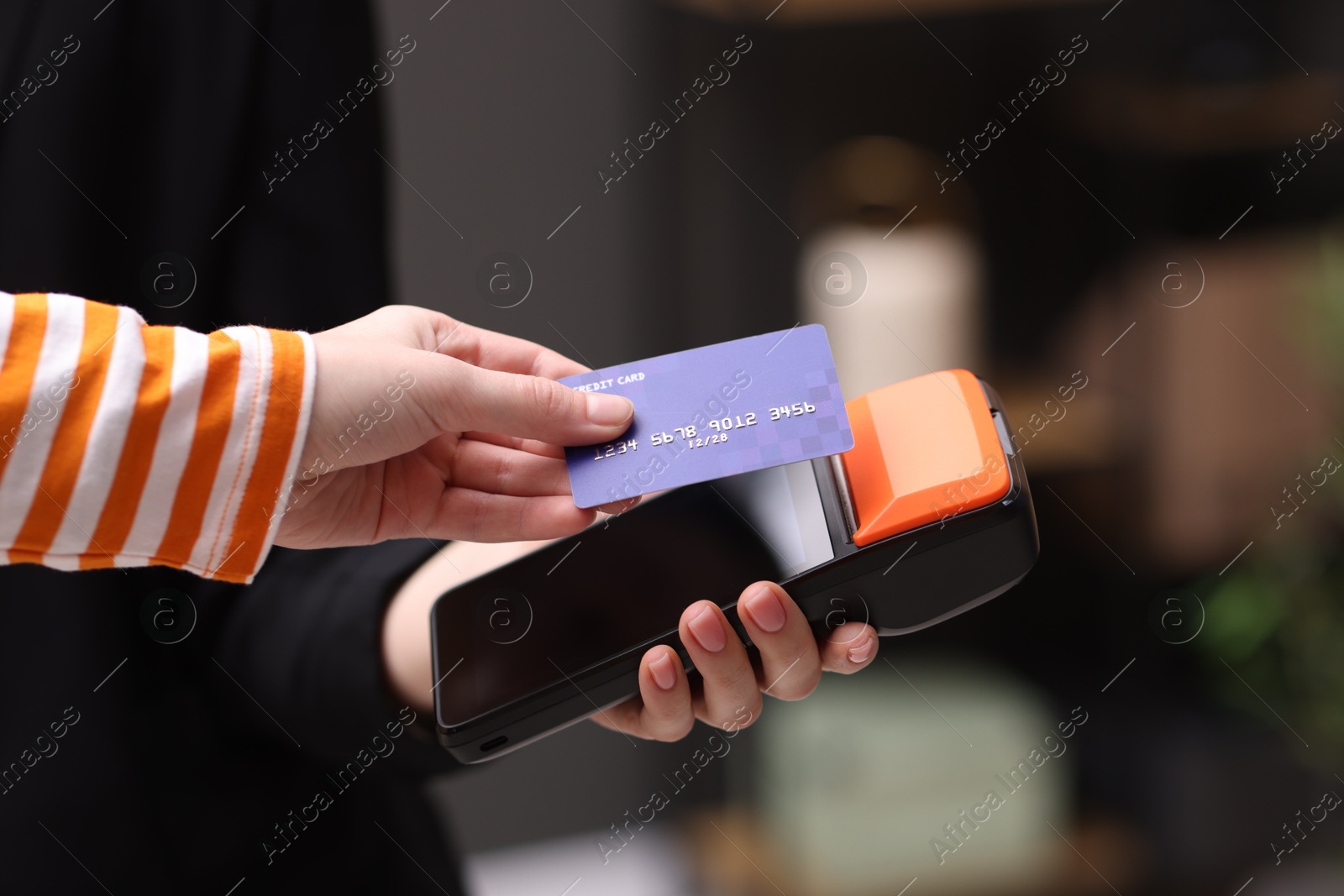 Photo of Woman paying with credit card via terminal against blurred background, closeup