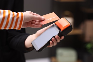 Photo of Woman paying with credit card via terminal against blurred background, closeup