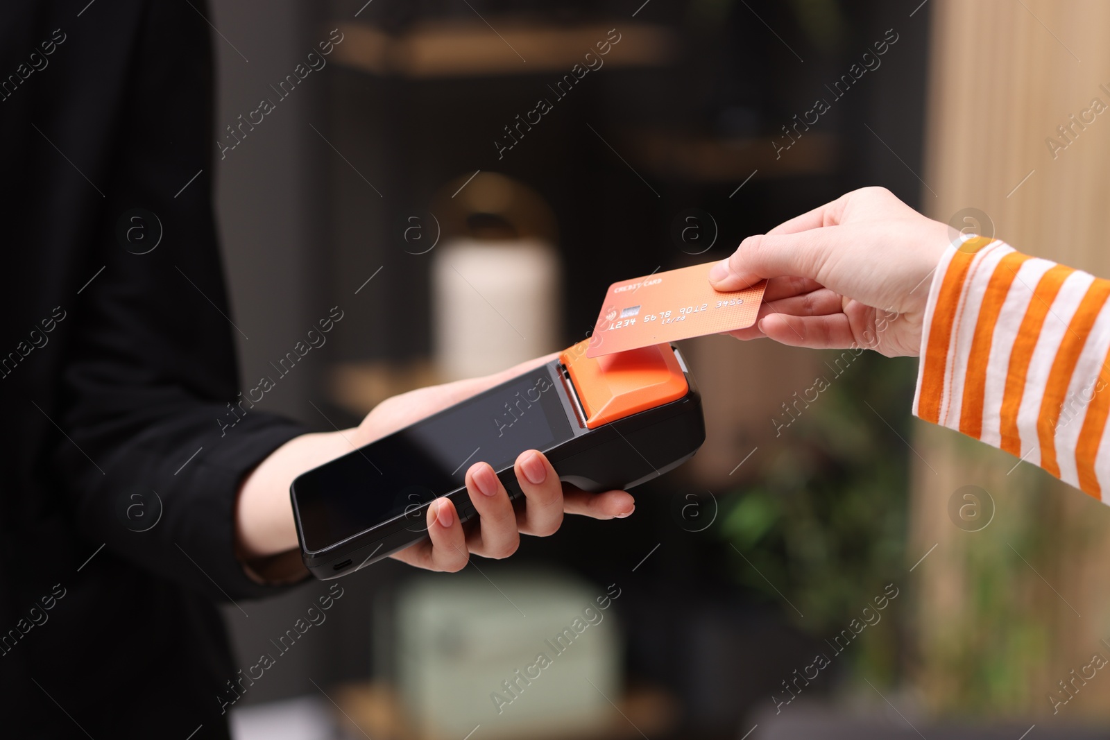 Photo of Woman paying with credit card via terminal against blurred background, closeup