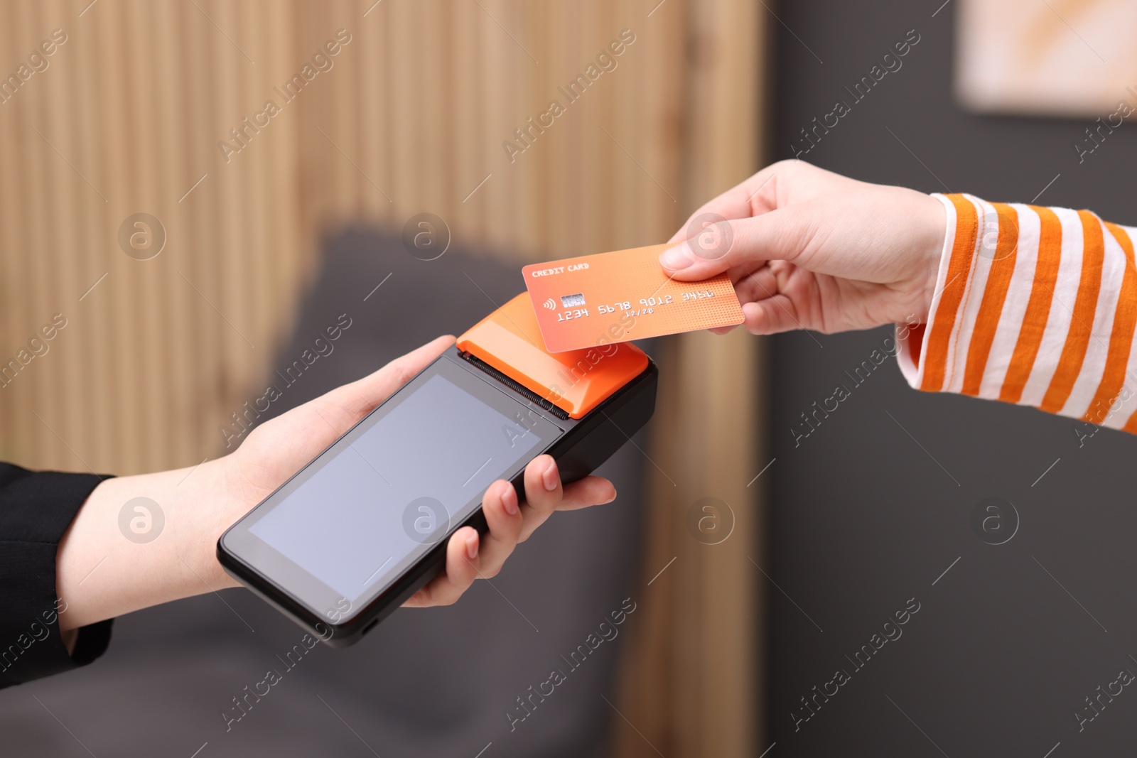 Photo of Woman paying with credit card via terminal against blurred background, closeup