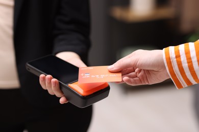 Photo of Woman paying with credit card via terminal against blurred background, closeup