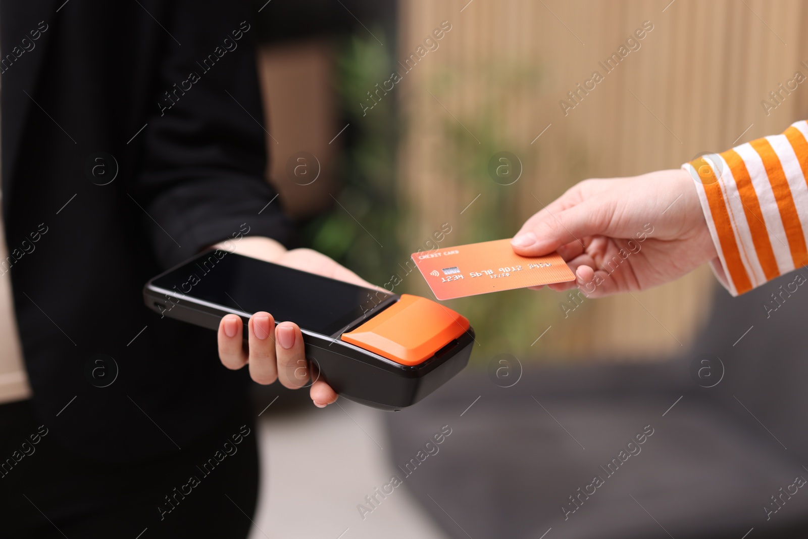 Photo of Woman paying with credit card via terminal against blurred background, closeup