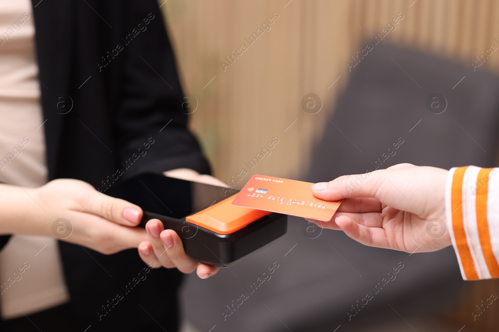 Photo of Woman paying with credit card via terminal against blurred background, closeup