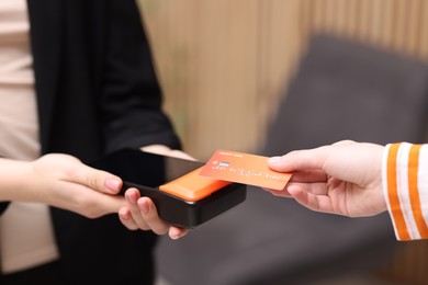 Photo of Woman paying with credit card via terminal against blurred background, closeup