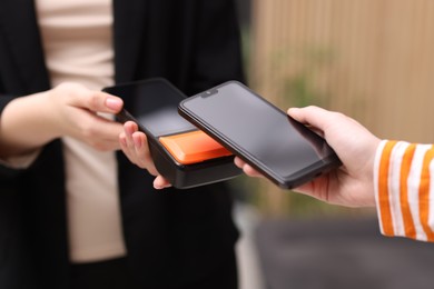 Photo of Woman paying with smartphone via terminal against blurred background, closeup