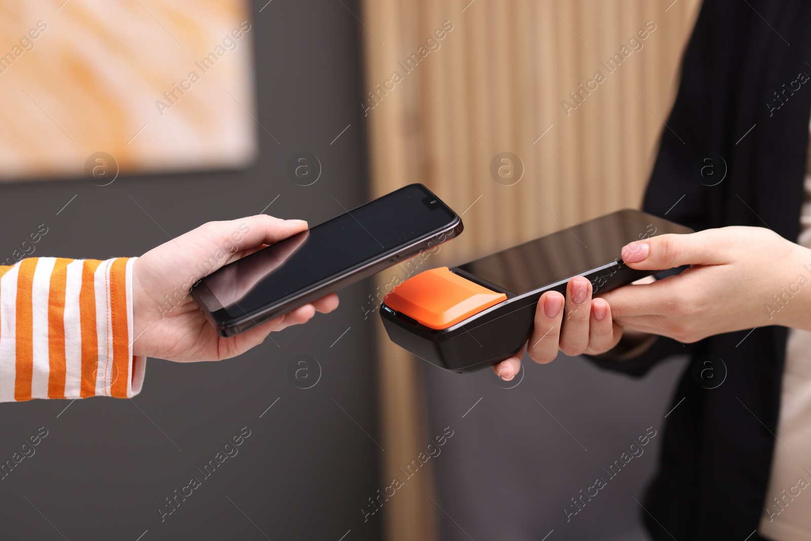 Photo of Woman paying with smartphone via terminal against blurred background, closeup