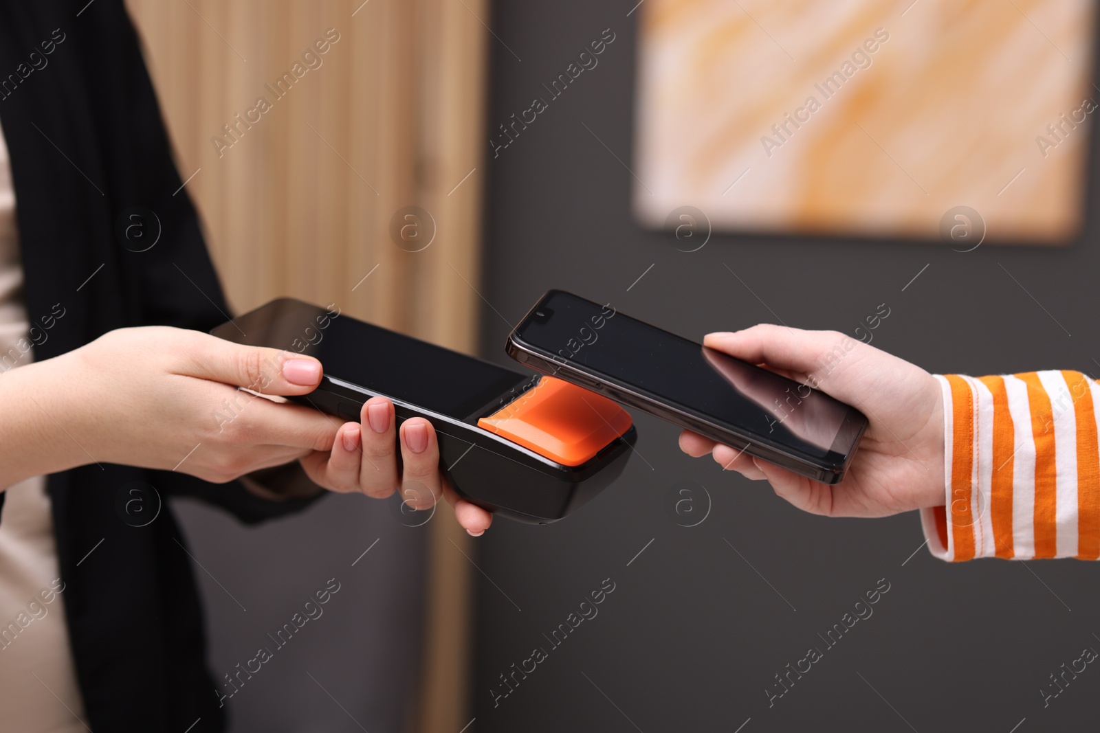 Photo of Woman paying with smartphone via terminal against blurred background, closeup