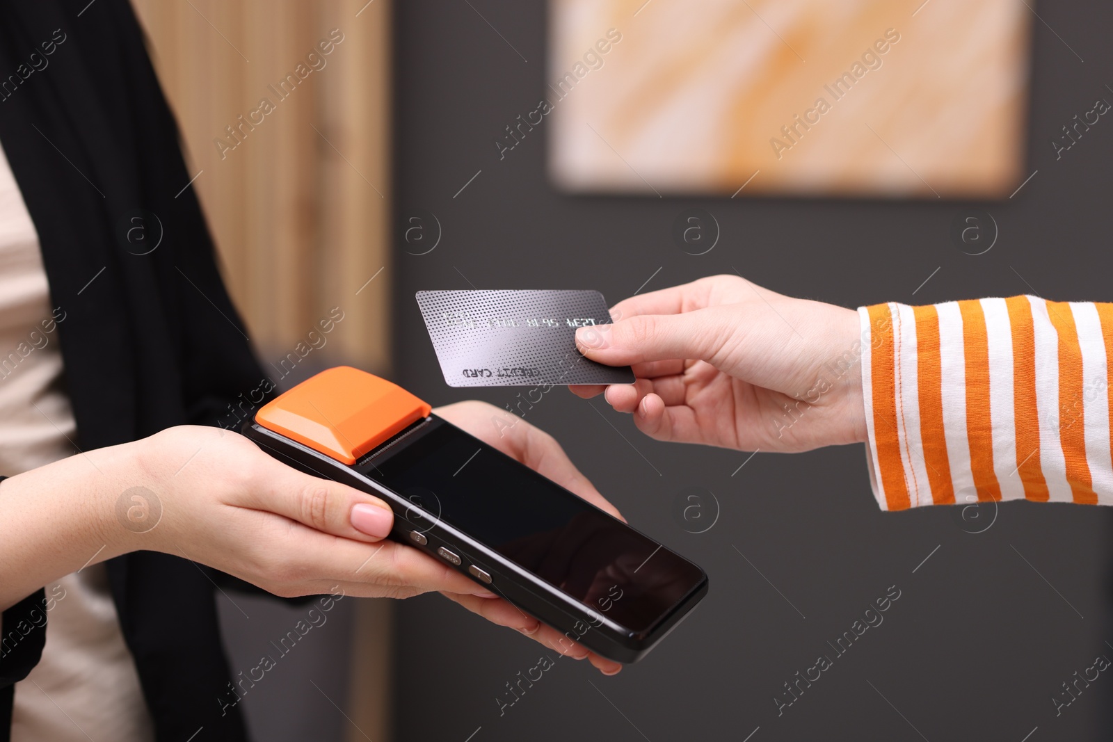 Photo of Woman paying with credit card via terminal against blurred background, closeup