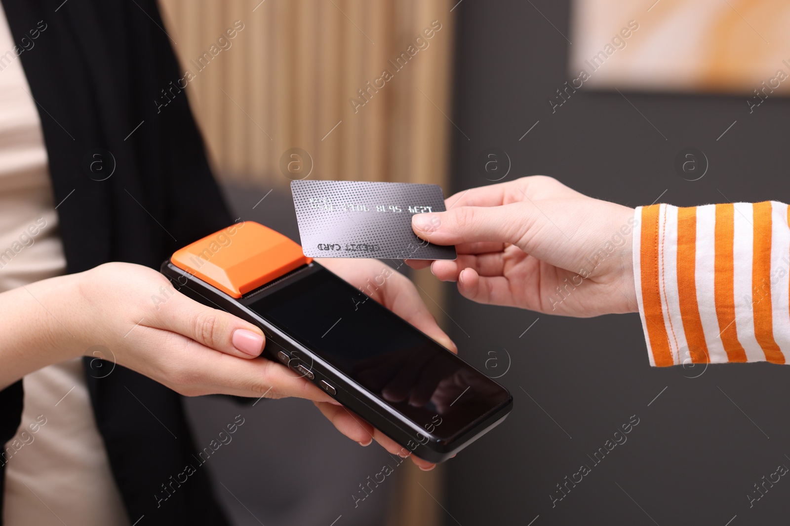 Photo of Woman paying with credit card via terminal against blurred background, closeup