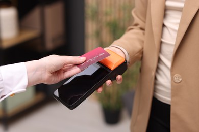 Photo of Woman paying with credit card via terminal against blurred background, closeup