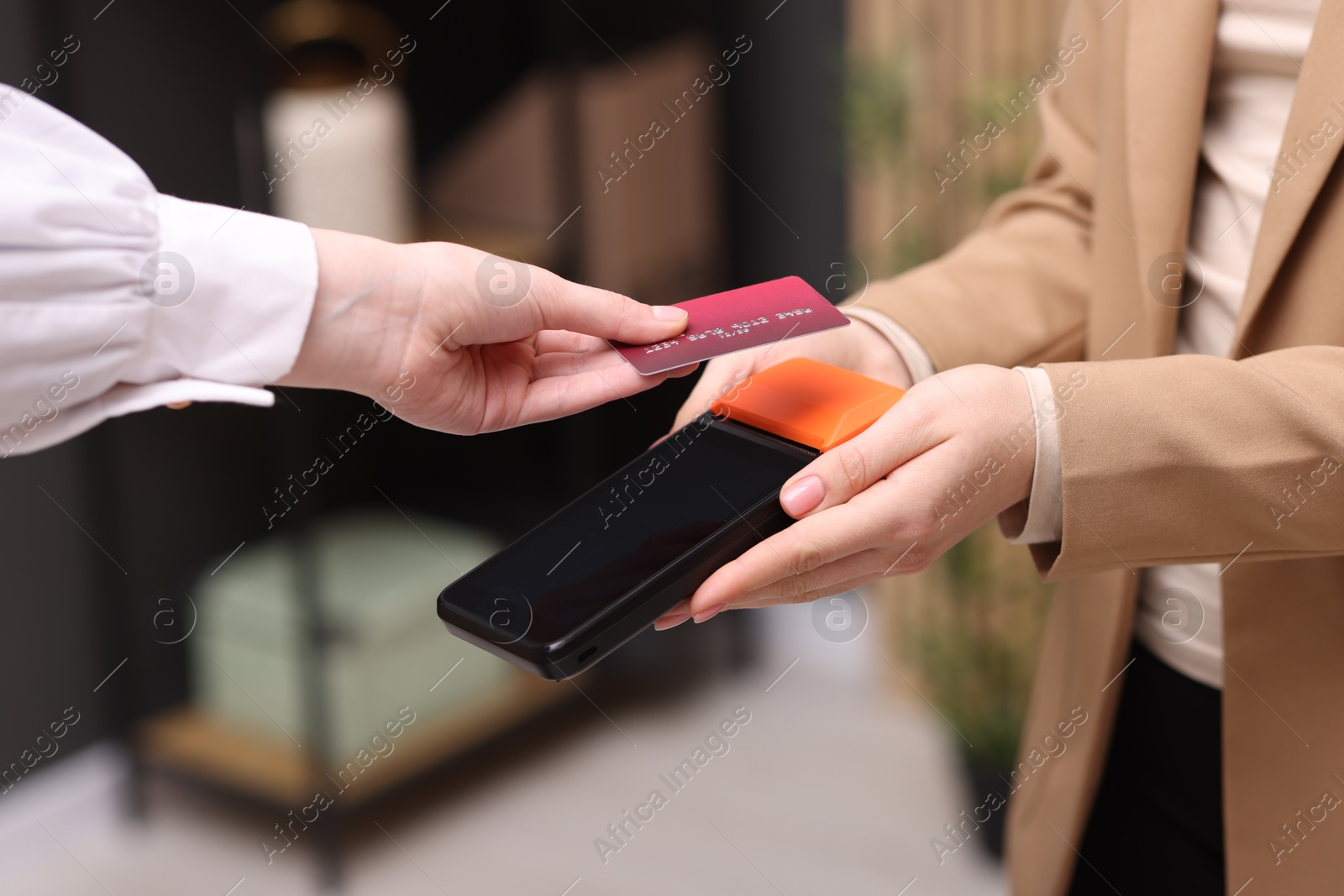 Photo of Woman paying with credit card via terminal against blurred background, closeup