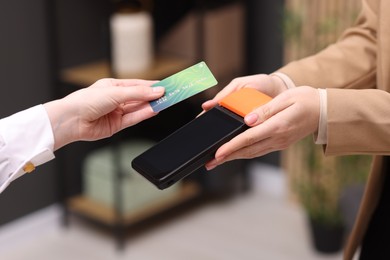 Photo of Woman paying with credit card via terminal against blurred background, closeup