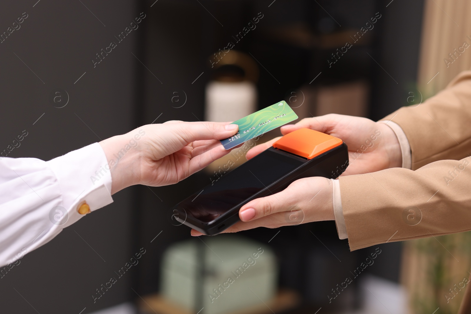 Photo of Woman paying with credit card via terminal against blurred background, closeup