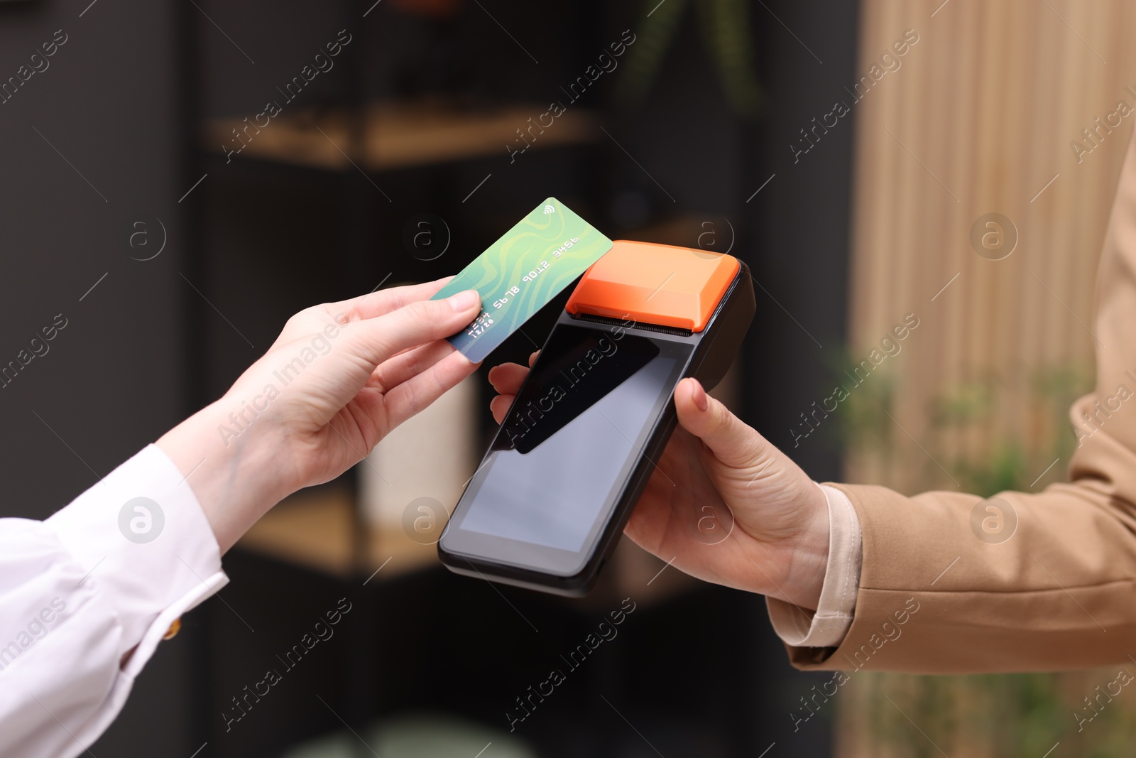 Photo of Woman paying with credit card via terminal against blurred background, closeup