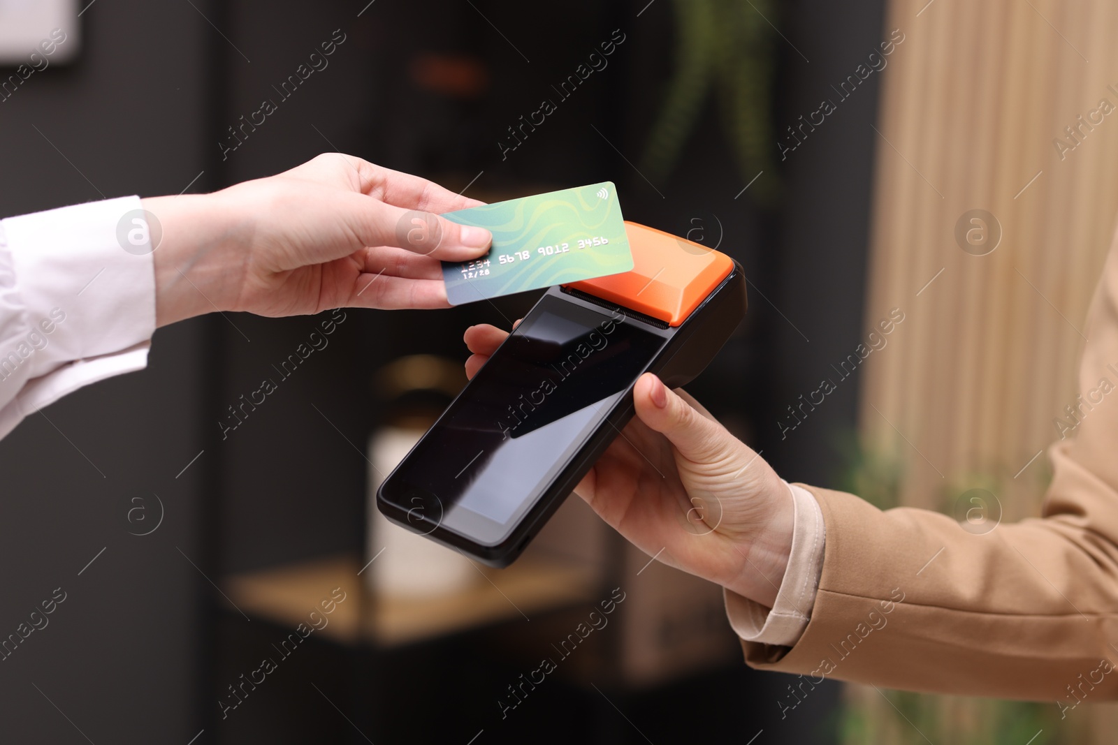 Photo of Woman paying with credit card via terminal against blurred background, closeup