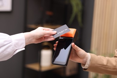 Photo of Woman paying with credit card via terminal against blurred background, closeup