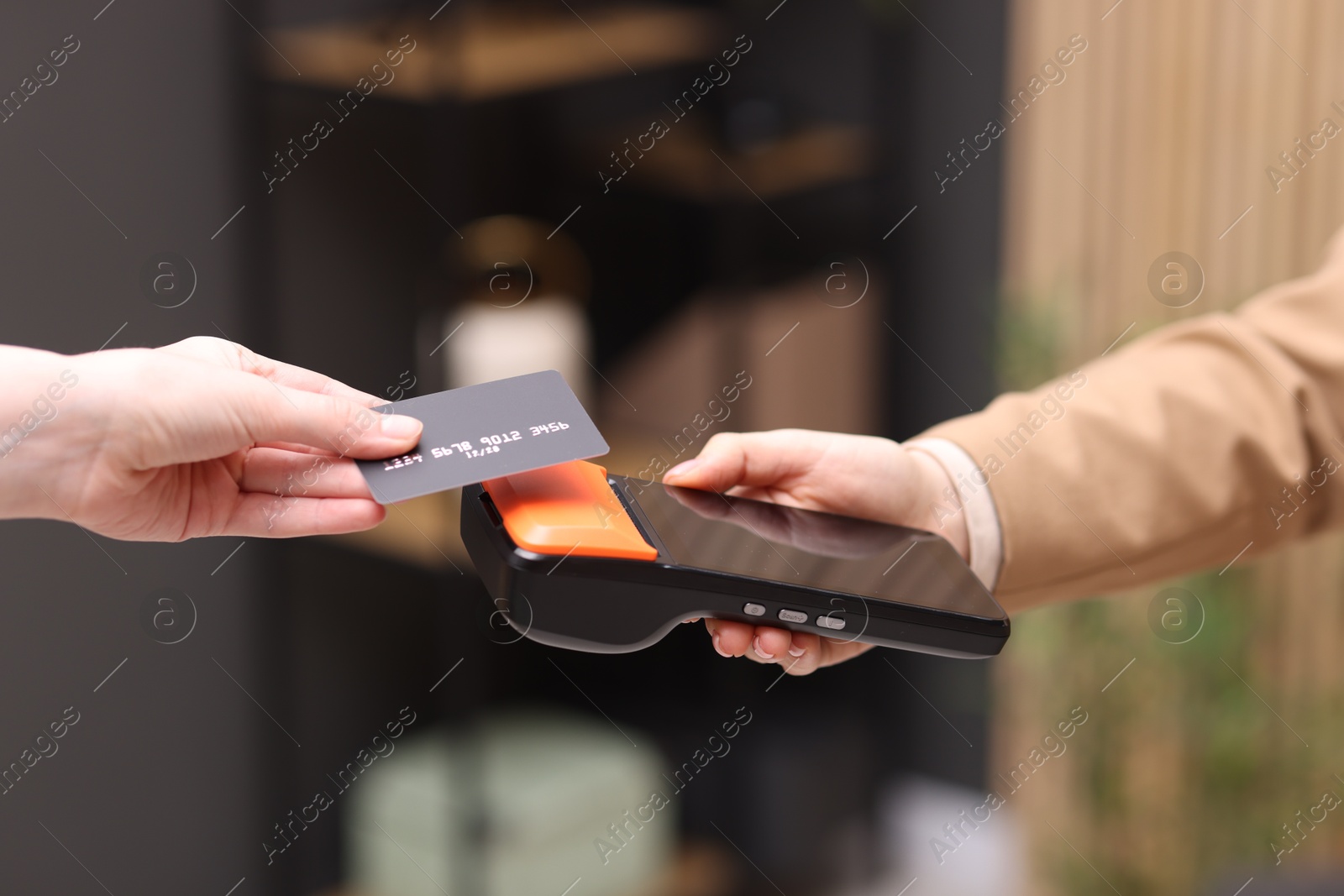 Photo of Woman paying with credit card via terminal against blurred background, closeup