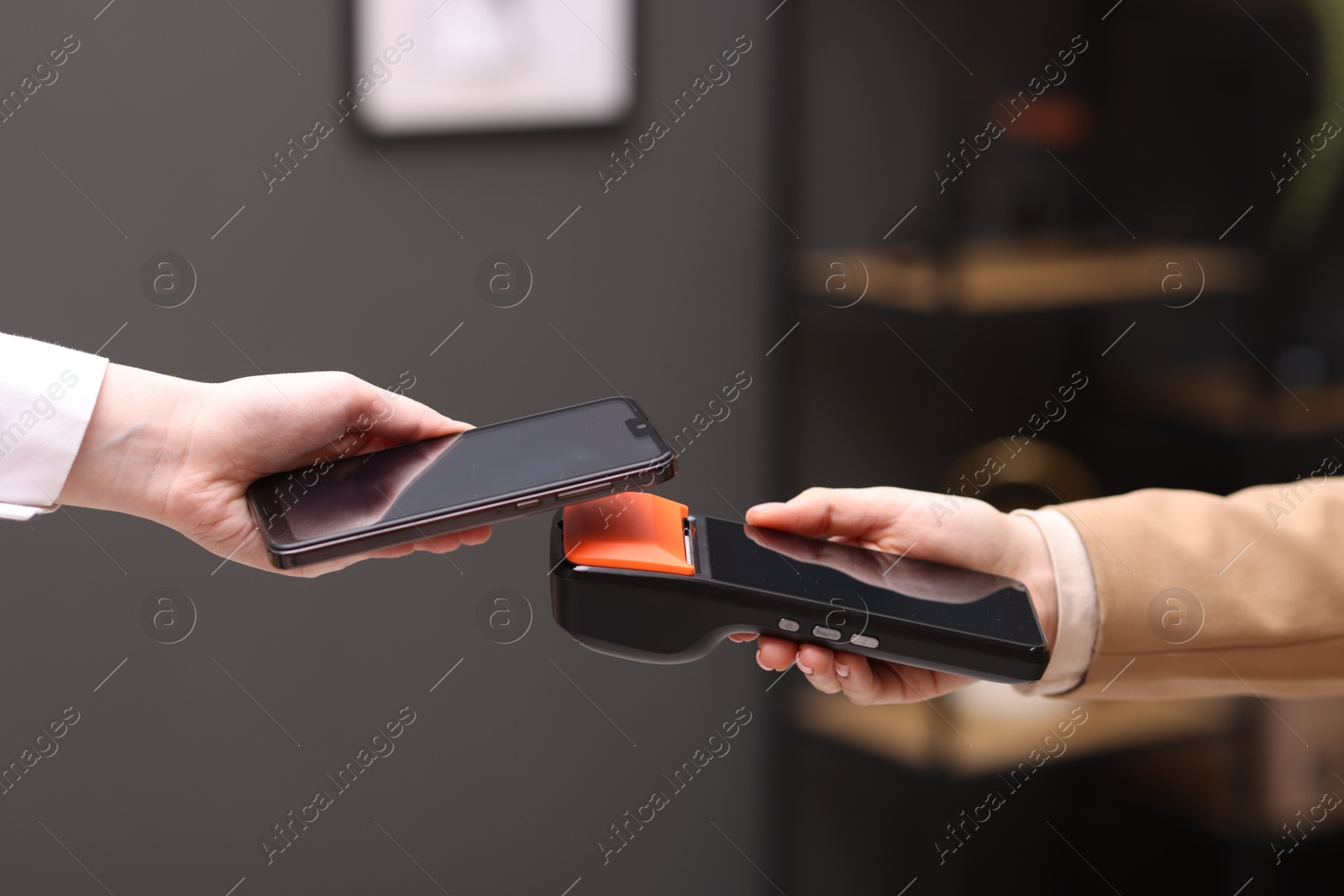 Photo of Woman paying with smartphone via terminal against blurred background, closeup