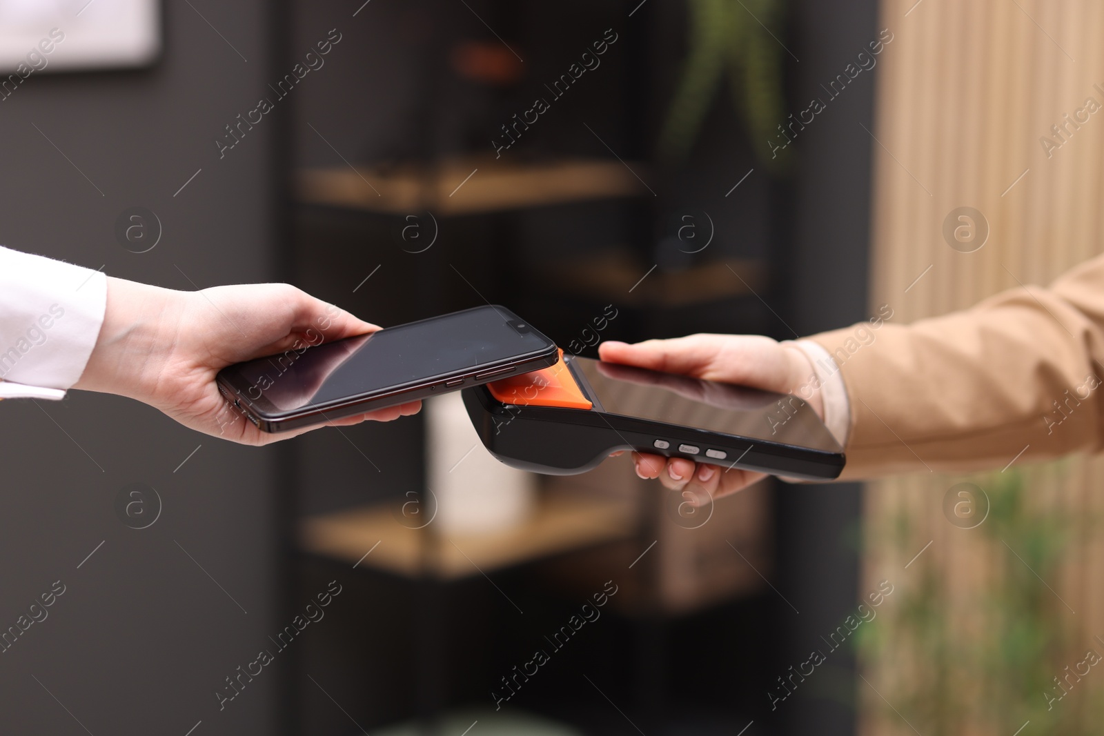 Photo of Woman paying with smartphone via terminal against blurred background, closeup