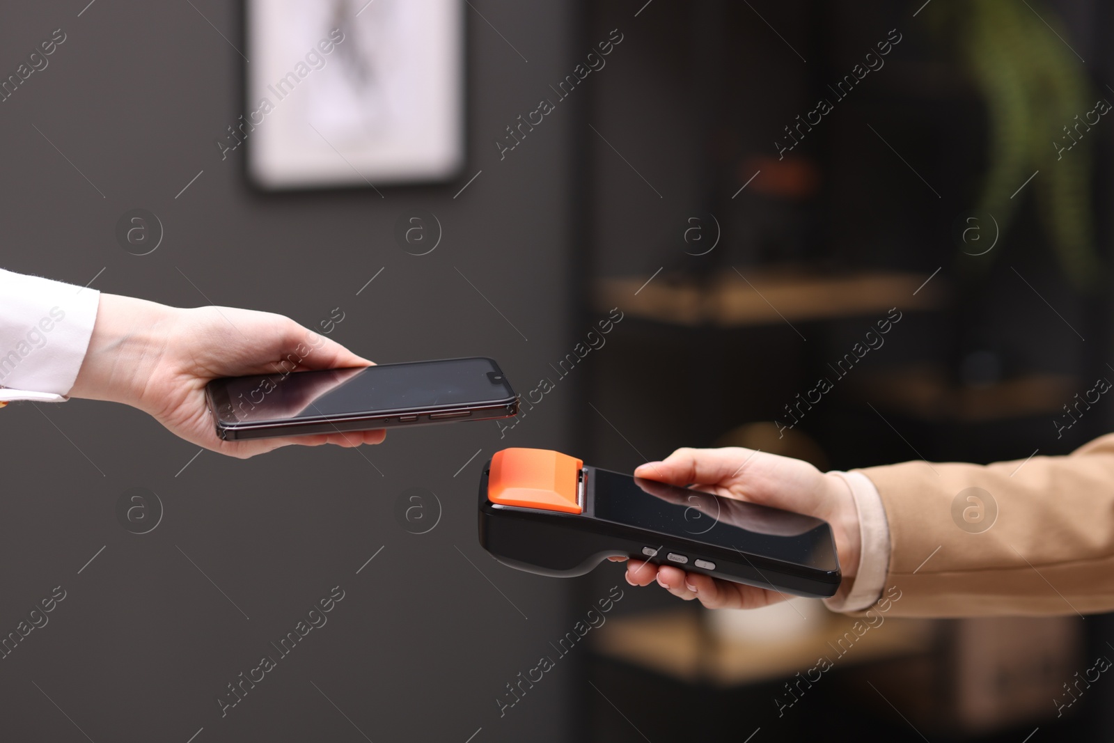 Photo of Woman paying with smartphone via terminal against blurred background, closeup