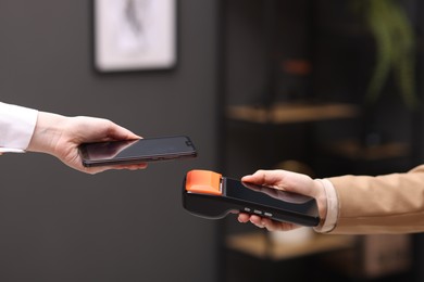 Photo of Woman paying with smartphone via terminal against blurred background, closeup