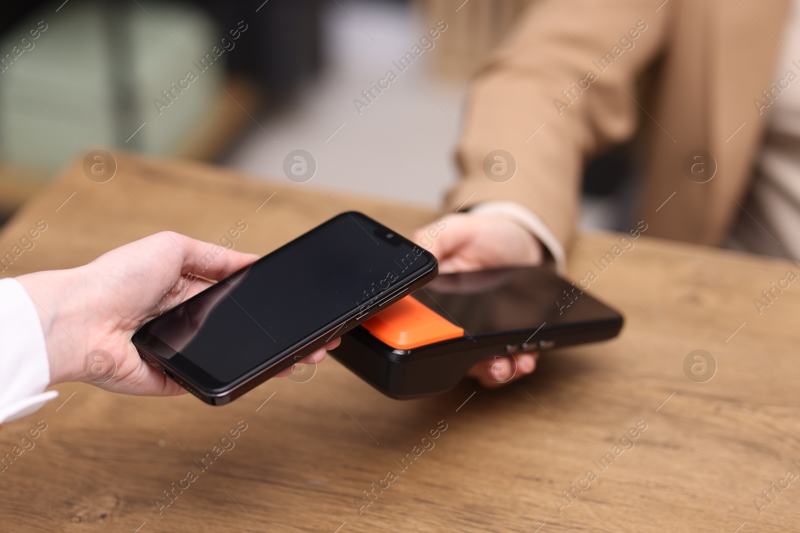 Photo of Woman paying with smartphone via terminal at wooden counter indoors, closeup