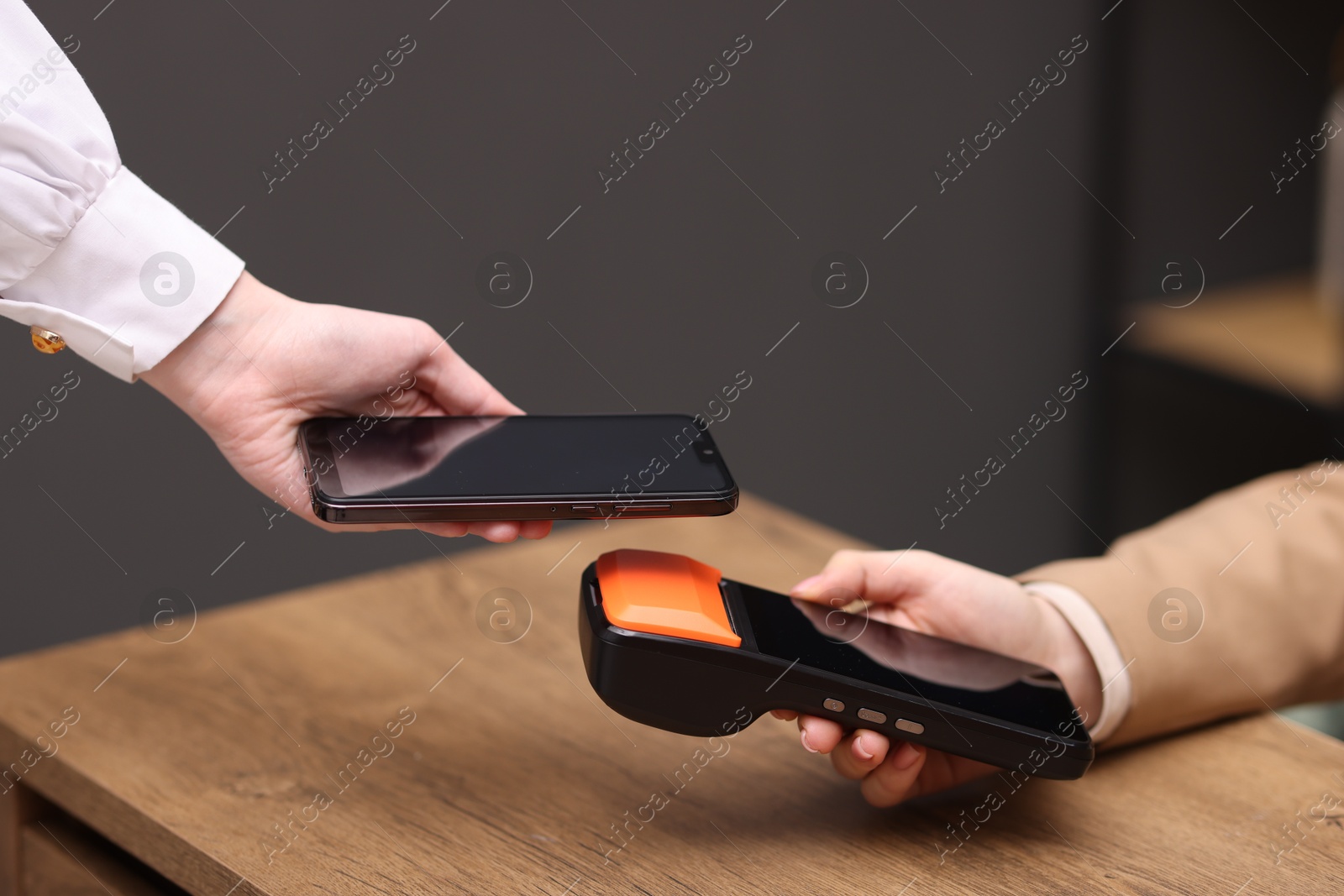 Photo of Woman paying with smartphone via terminal at wooden counter indoors, closeup