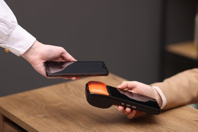 Photo of Woman paying with smartphone via terminal at wooden counter indoors, closeup