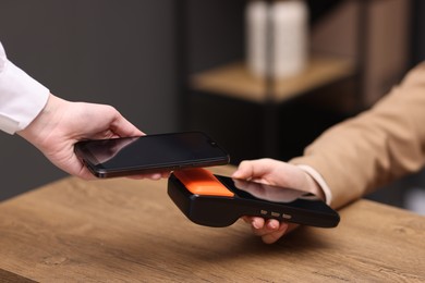 Photo of Woman paying with smartphone via terminal at wooden counter indoors, closeup