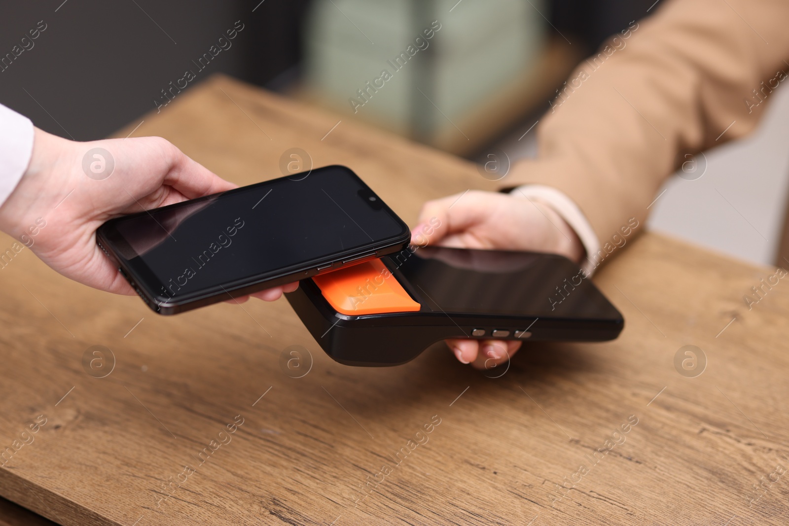 Photo of Woman paying with smartphone via terminal at wooden counter indoors, closeup