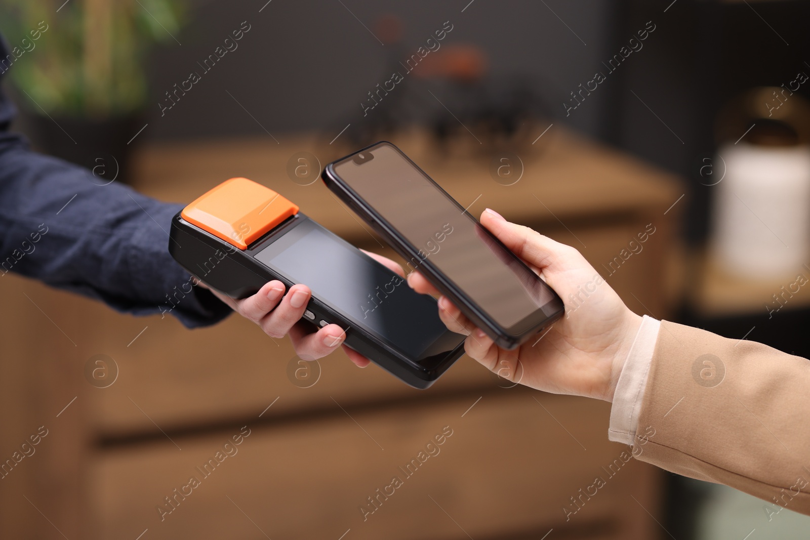 Photo of Woman paying with smartphone via terminal against blurred background, closeup