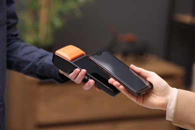 Woman paying with smartphone via terminal against blurred background, closeup