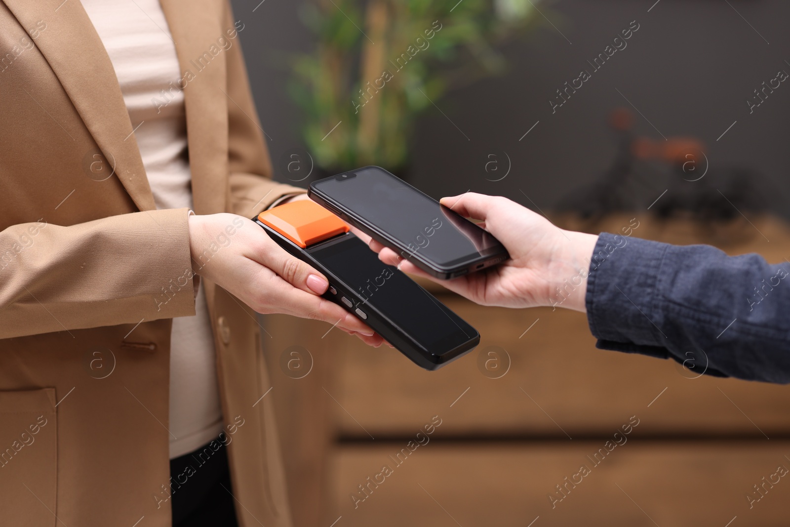 Photo of Woman paying with smartphone via terminal against blurred background, closeup