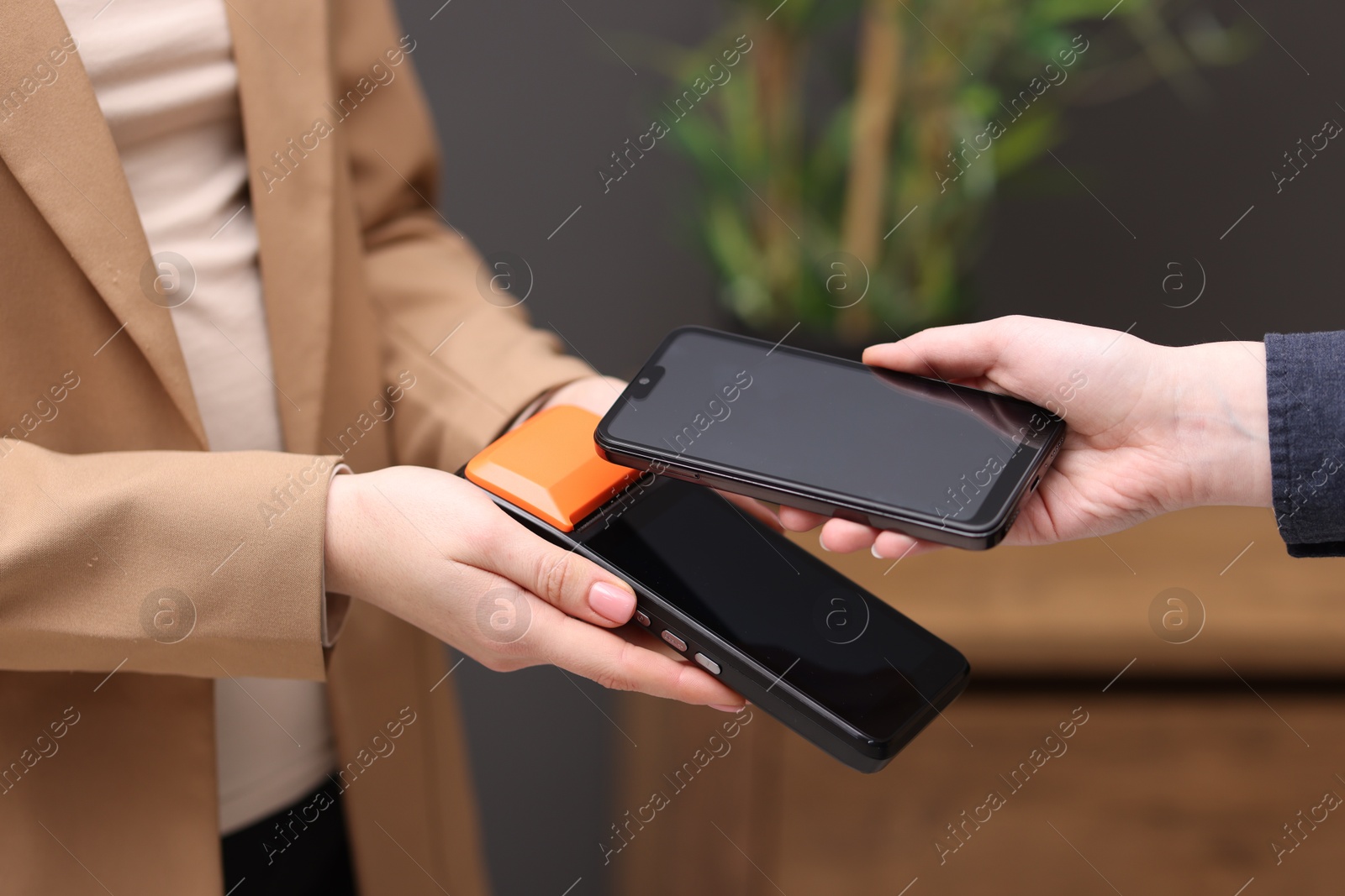 Photo of Woman paying with smartphone via terminal against blurred background, closeup