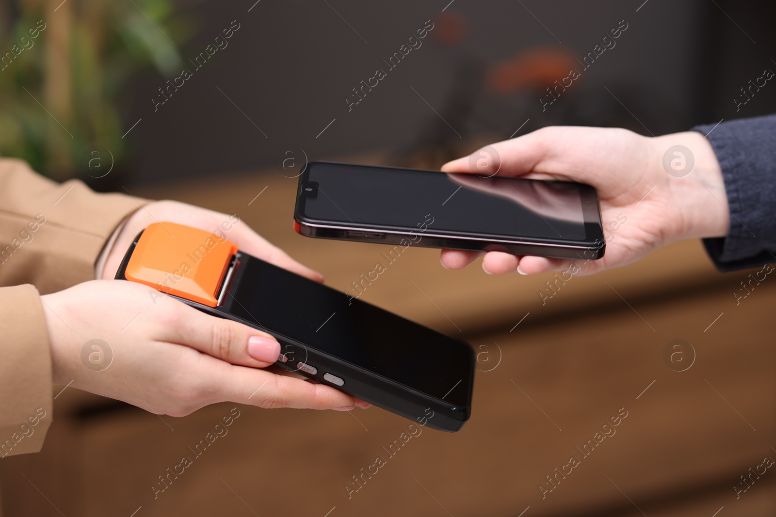 Photo of Woman paying with smartphone via terminal against blurred background, closeup