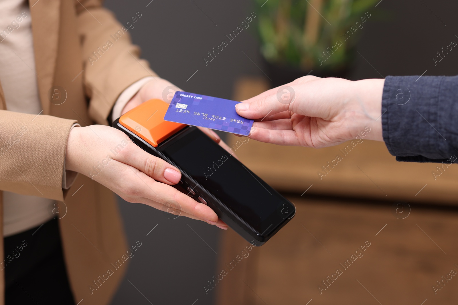 Photo of Woman paying with credit card via terminal against blurred background, closeup