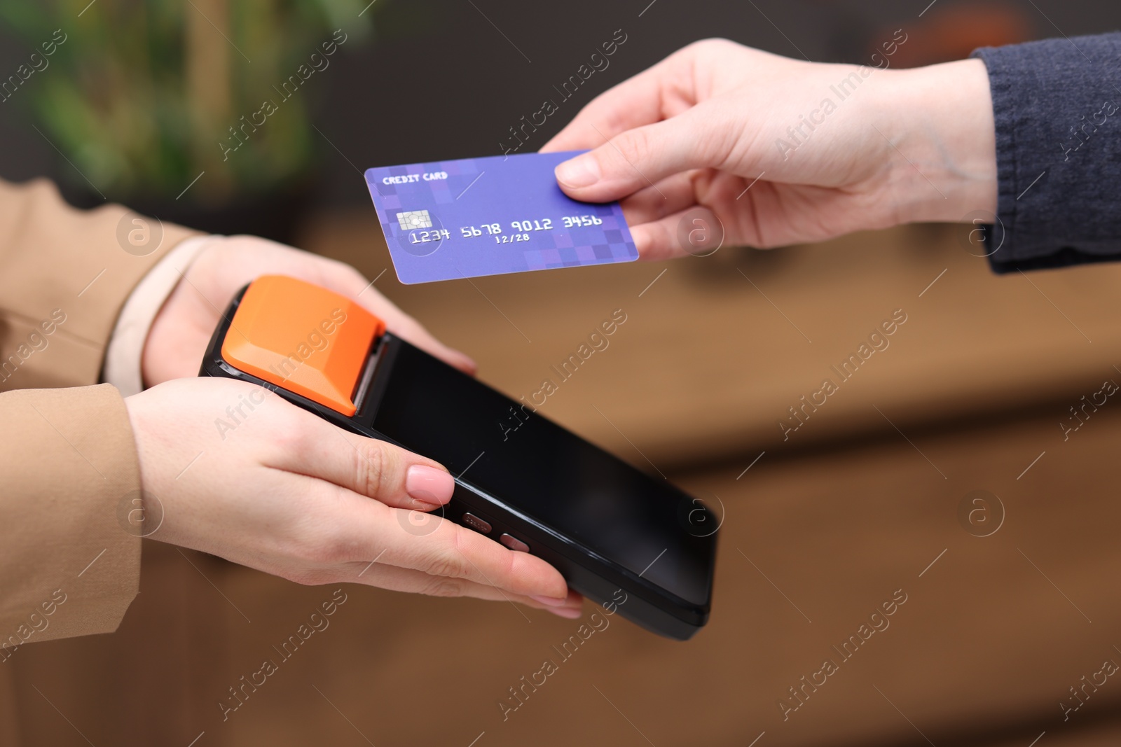 Photo of Woman paying with credit card via terminal against blurred background, closeup