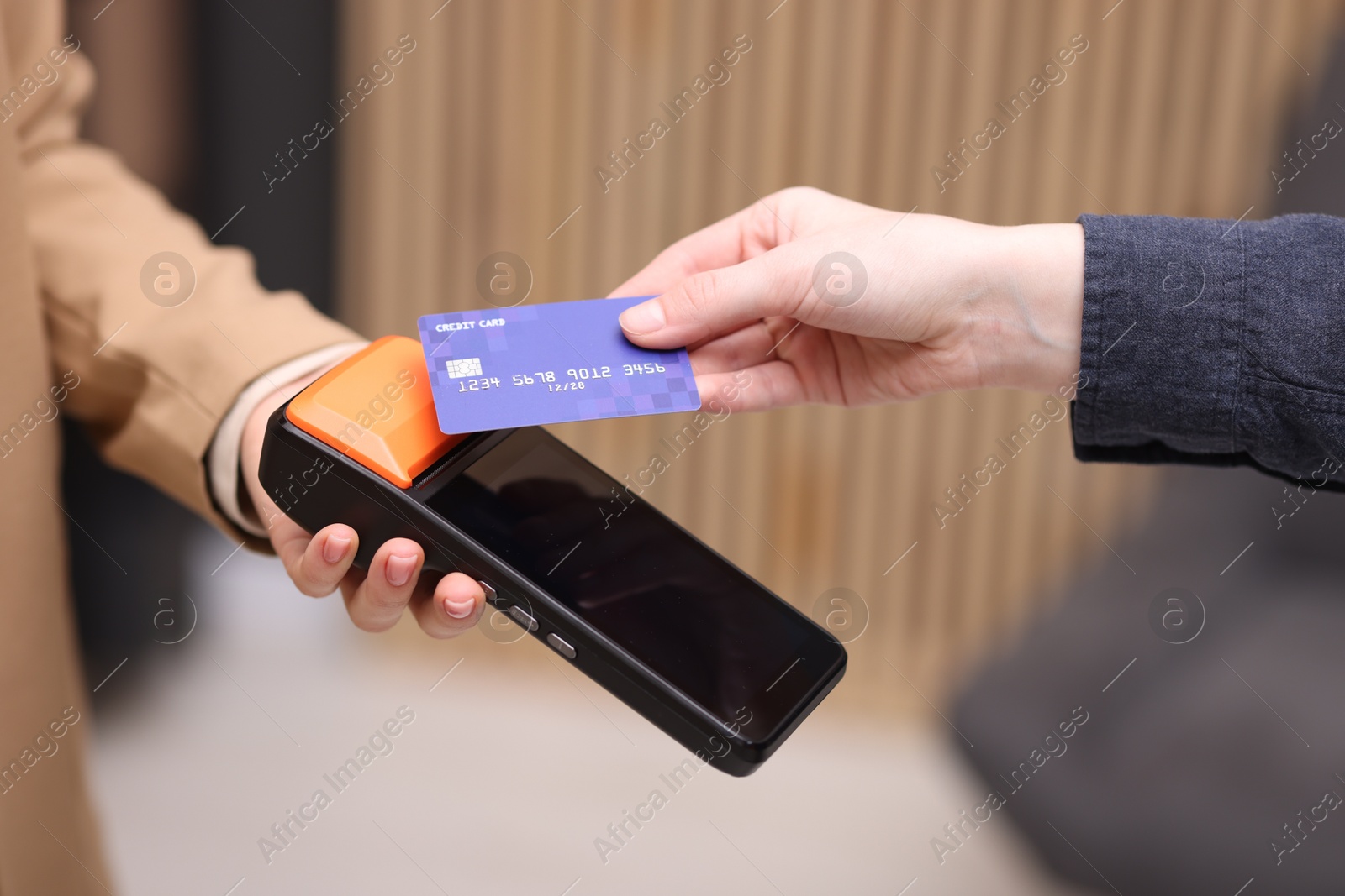 Photo of Woman paying with credit card via terminal against blurred background, closeup