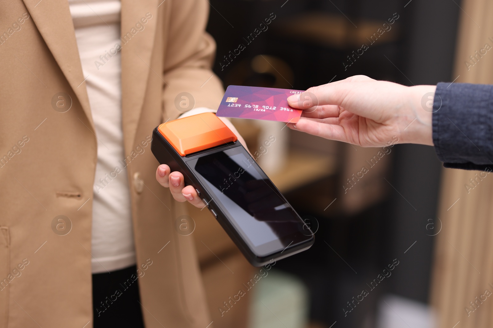 Photo of Woman paying with credit card via terminal against blurred background, closeup