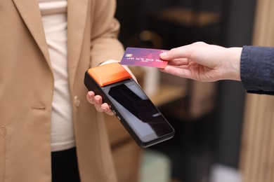 Photo of Woman paying with credit card via terminal against blurred background, closeup