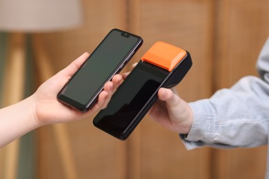 Photo of Woman paying with smartphone via terminal against blurred background, closeup